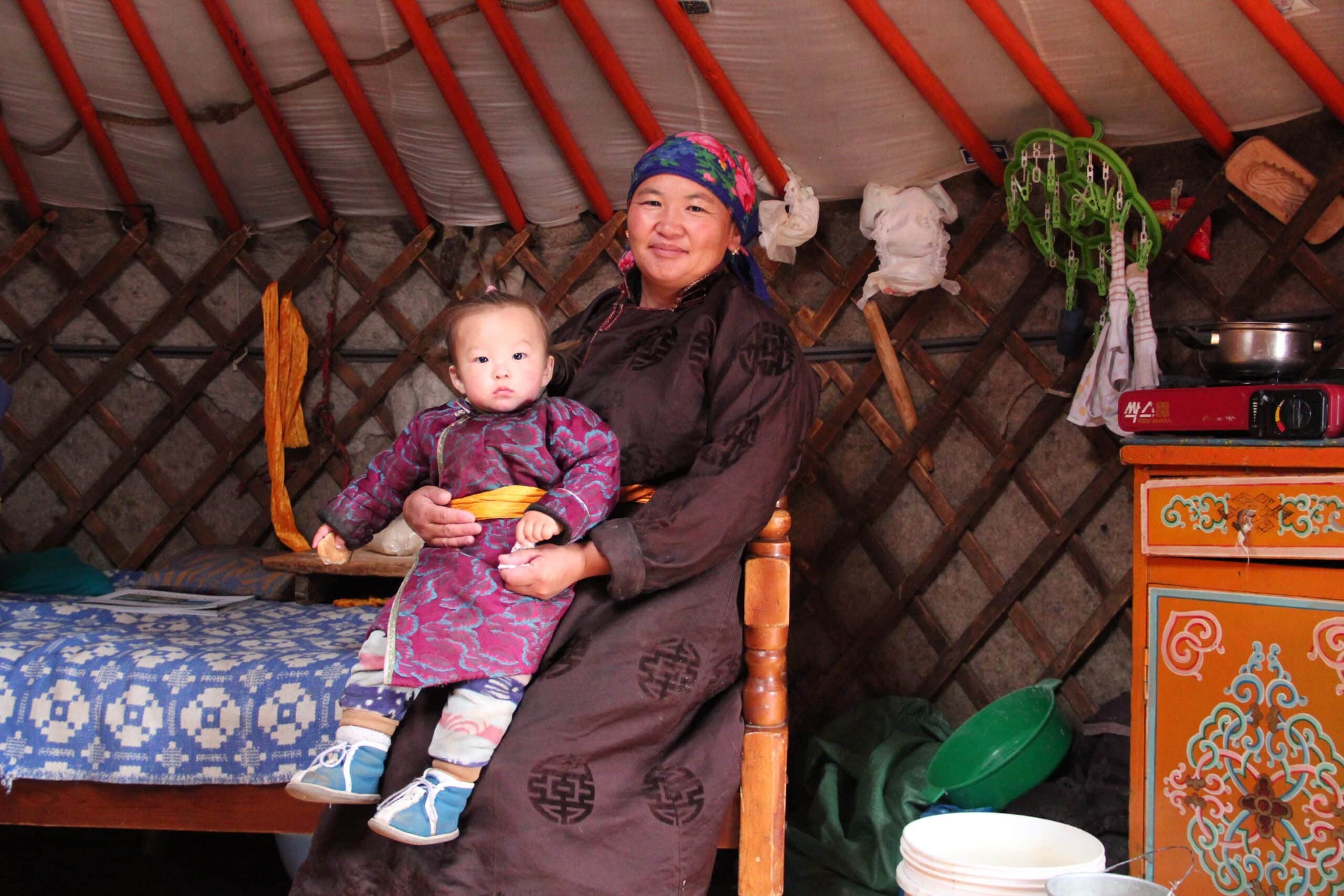 A Mongolian nomad woman and child sit in their ger