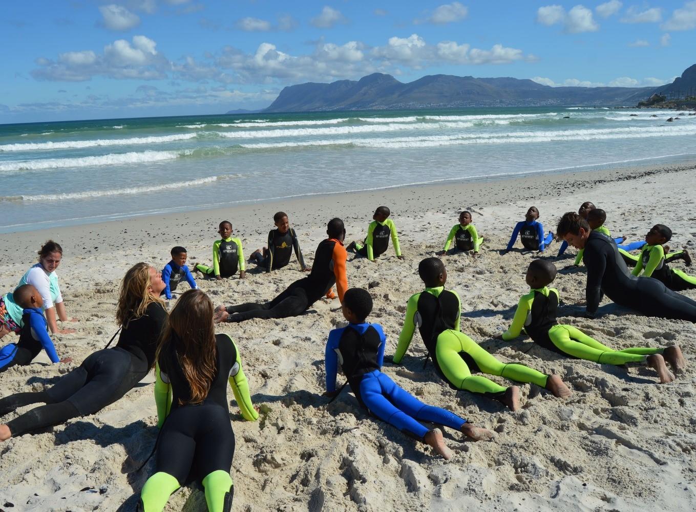 Volunteers stretch with the children at the Surfing Project in South Africa Projects Abroad volunteers stretching on the beach with children and gaining new skills at a Surfing Project