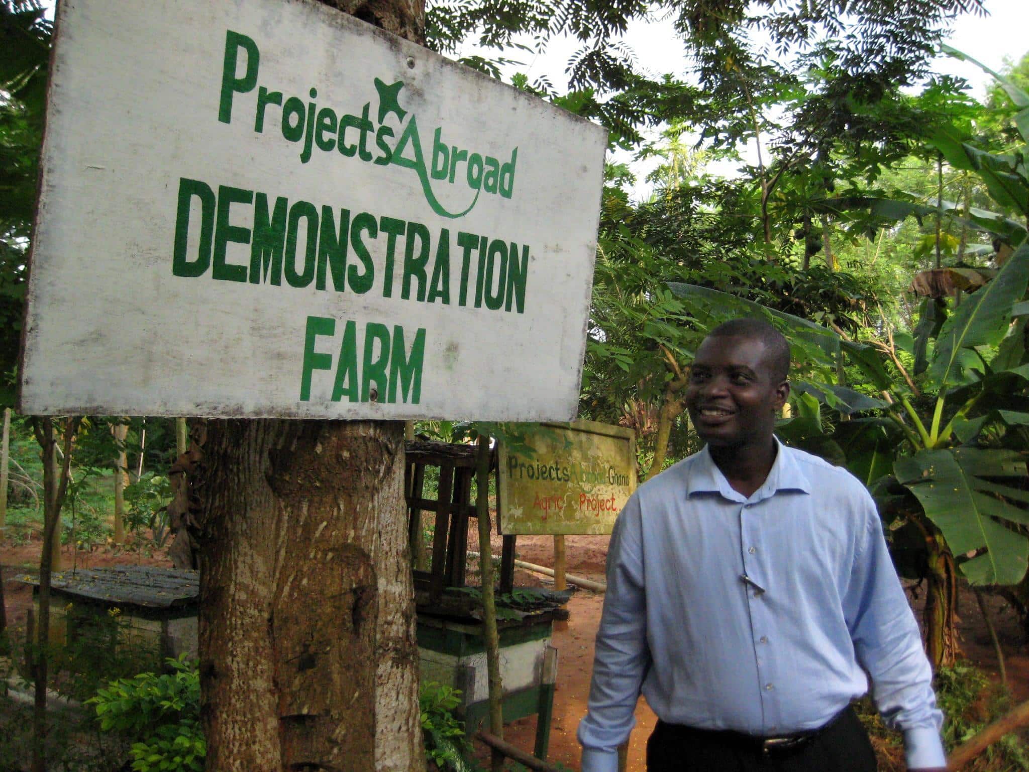 Man stands by sign for demonstration farm in Ghana