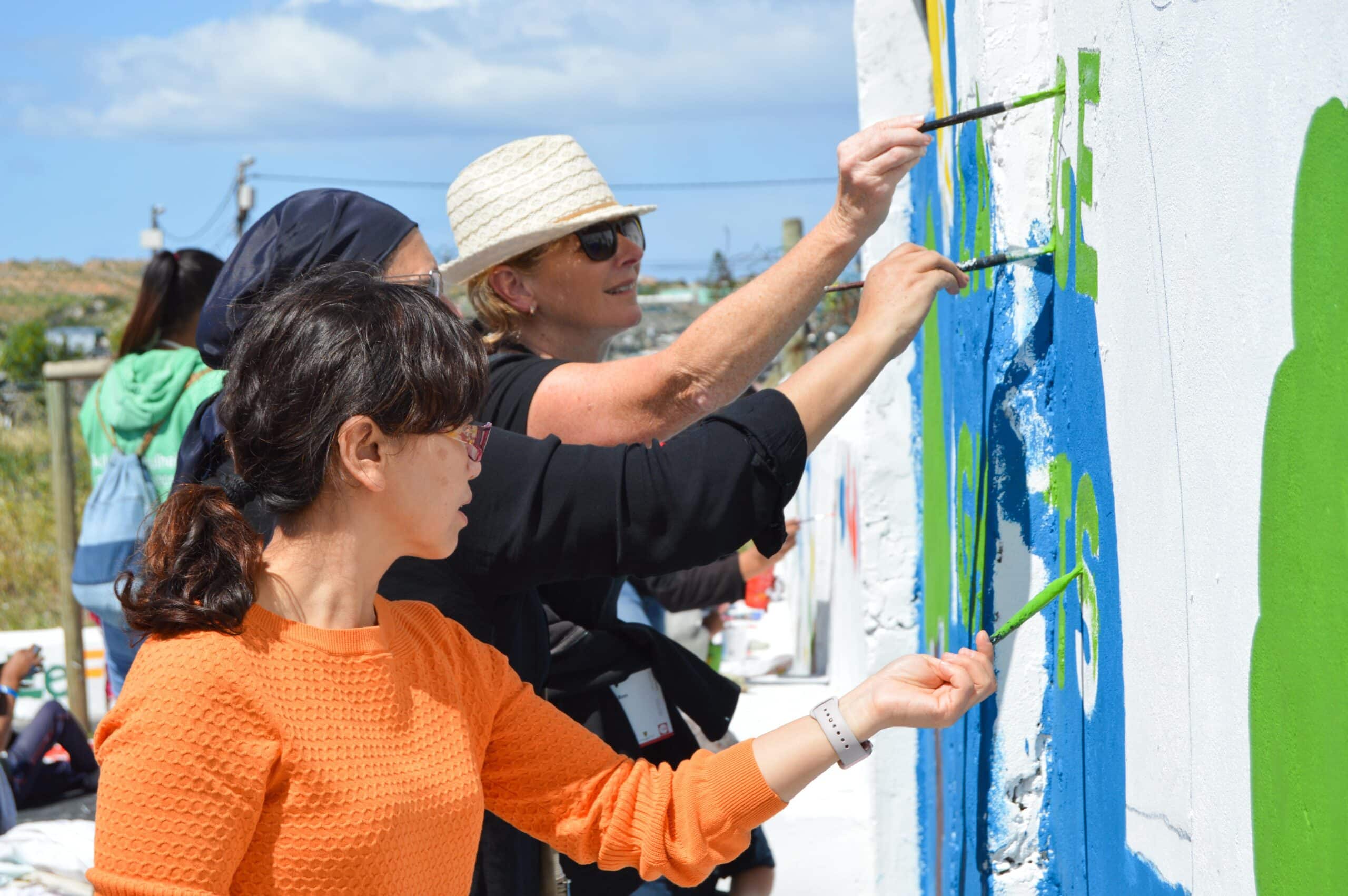 Volunteers work together to paint an educational mural while volunteering overseas on a project with no requirements.