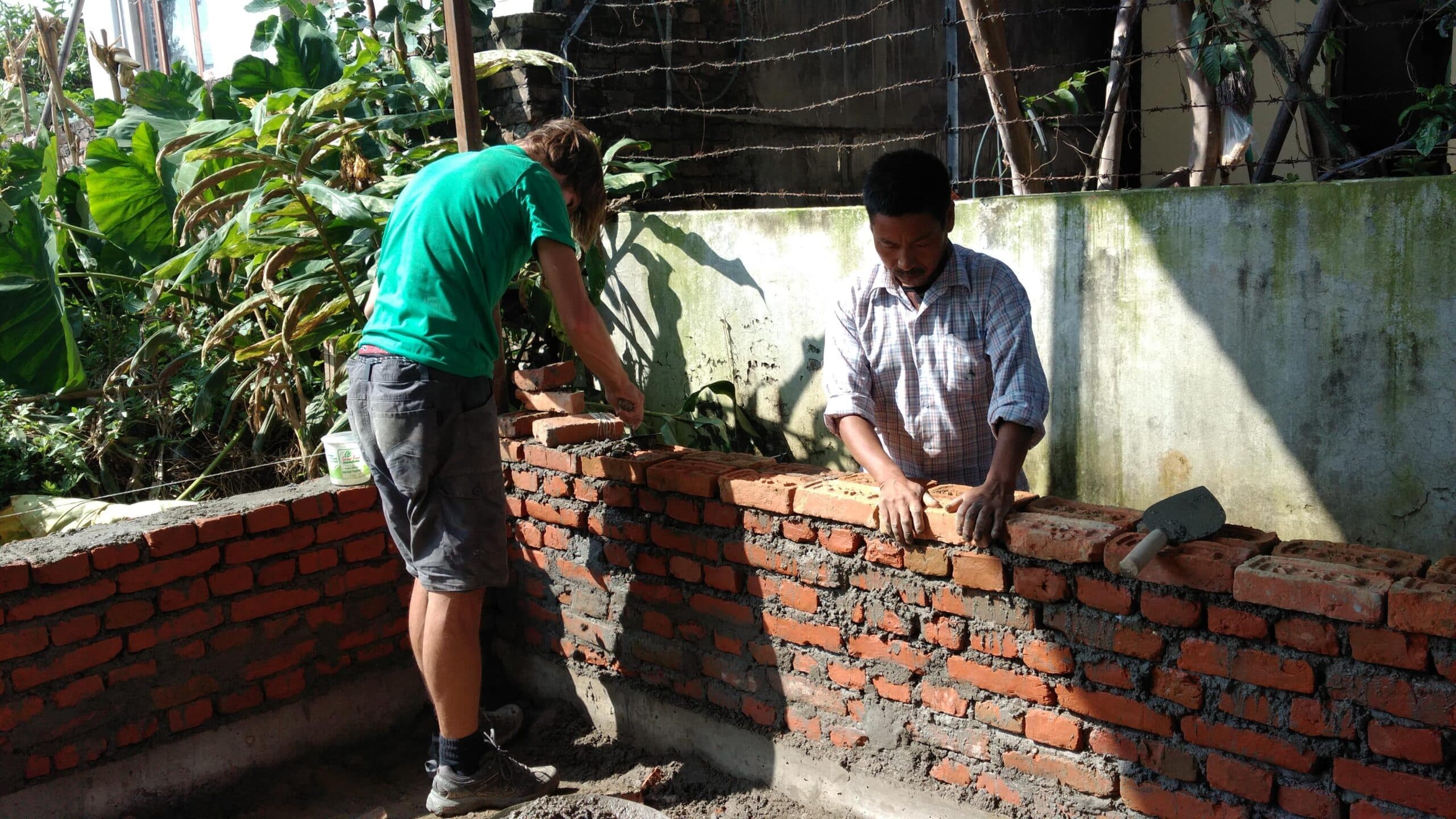 A volunteer is helping a local builder with building a wall during the Building Project in Nepal