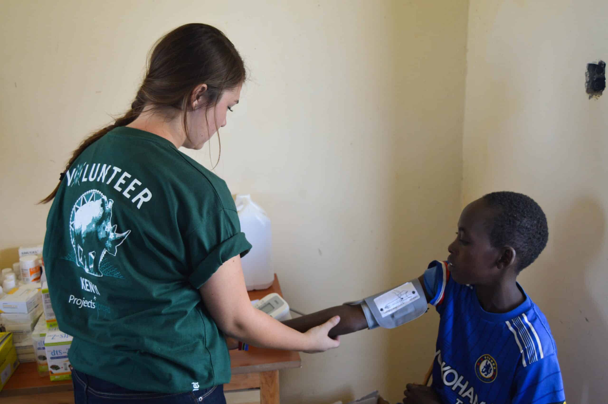 A teenage volunteer doing a medical internship with Projects Abroad in Kenya takes the blood pressure to a child.