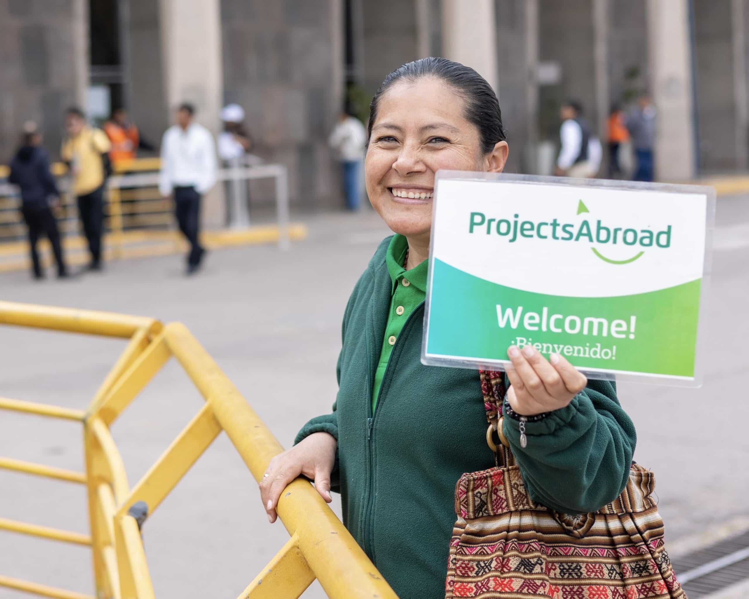 Woman holding a 'Projects Abroad Welcome' sign outside an airport